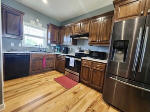 A kitchen with wooden cabinets, stainless steel appliances, a dishwasher, a water dispenser, and a red mat on the floor.