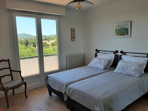 Ein Schlafzimmer mit zwei Betten, einem Sessel, einem Heizkörper, einem Fenster mit Blick und einem gerahmten Bild an der Wand.
