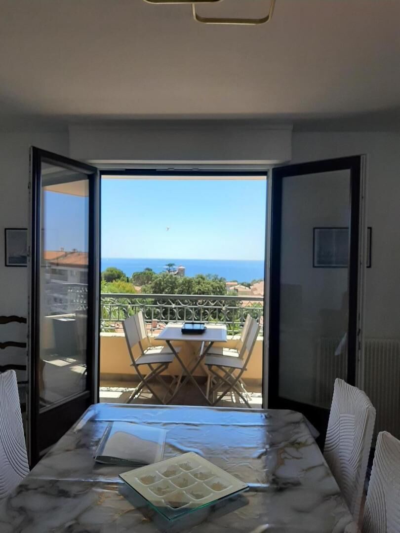 A room with a marble table, chairs, and a view of the sea through an open door.