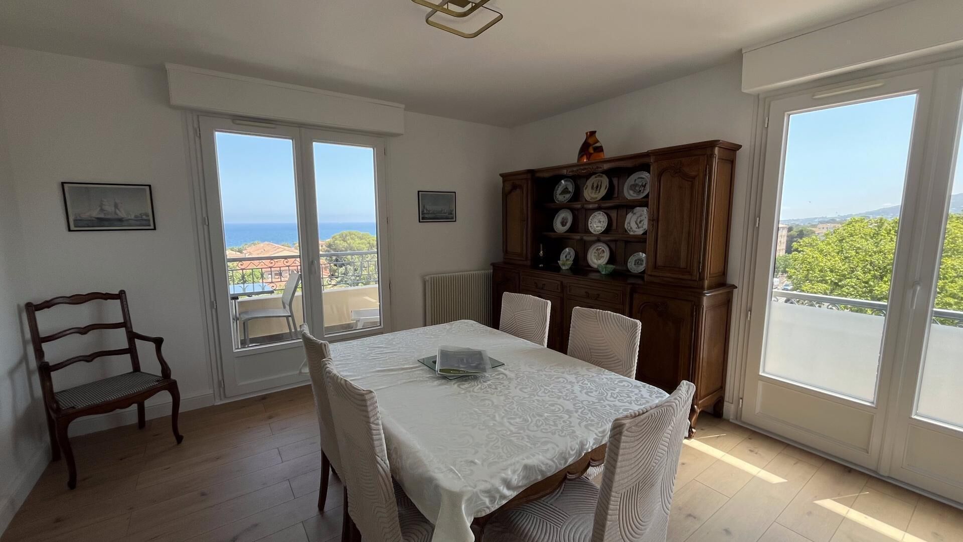 Un comedor con una mesa, sillas, un armario con platos y vistas al mar.