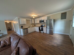 A modern kitchen with white cabinets, stainless steel appliances, and a wooden floor.