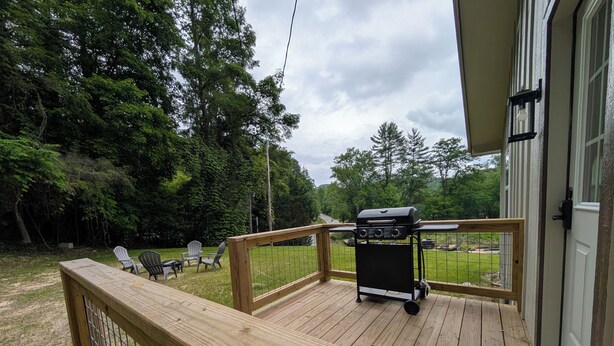 Eine Holzterrasse mit Grill, Stühlen und Blick auf ein Waldgebiet.