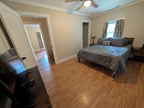 A bedroom with a bed, a ceiling fan, a window with curtains, and a door leading to another room.