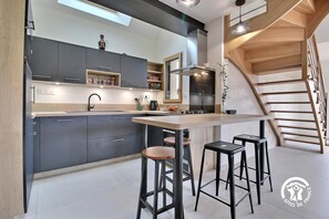 A modern kitchen with dark cabinets, a wooden island, and bar stools. - La Petite Casa de Silz (ARZAL)