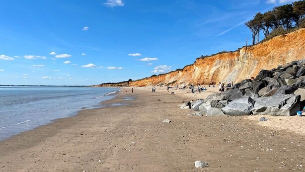 Een strand met een rotsachtige klif en een helderblauwe lucht.