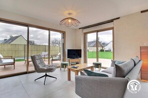 A spacious living room with a large TV, comfortable seating, and a view of the backyard through large sliding glass doors. - La Petite Casa de Silz (ARZAL)