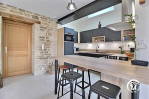 A modern kitchen with a stone wall, wooden door, and a bar area with stools. - La Petite Casa de Silz (ARZAL)