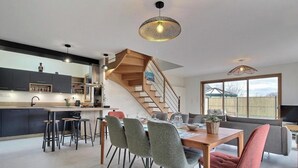 Een moderne keuken met een centraal eiland, een eethoek met een houten tafel en stoelen, en een trap naar een hoger niveau.
