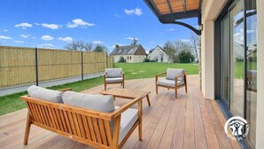 Een houten terras met buitenmeubilair, een overdekt gedeelte en een uitzicht op huizen in de verte.