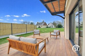A wooden deck with outdoor furniture, a covered area, and a view of houses in the background. - La Petite Casa de Silz (ARZAL)