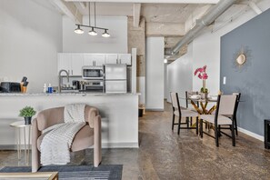 A modern kitchen with white cabinets, a central island, and a dining area with a table and chairs. - 2BR Riverfront District Loft | Near Power & Light (Kansas City)