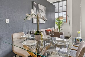 A modern dining area with a glass table, white plates, and a vase of white flowers. - Urban River Market Escape | 2BR, Sleeps 6 (Kansas City)