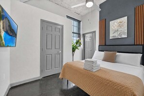 Een moderne hotelkamer met een bed, een groot raam, een deur en een schilderij aan de muur.