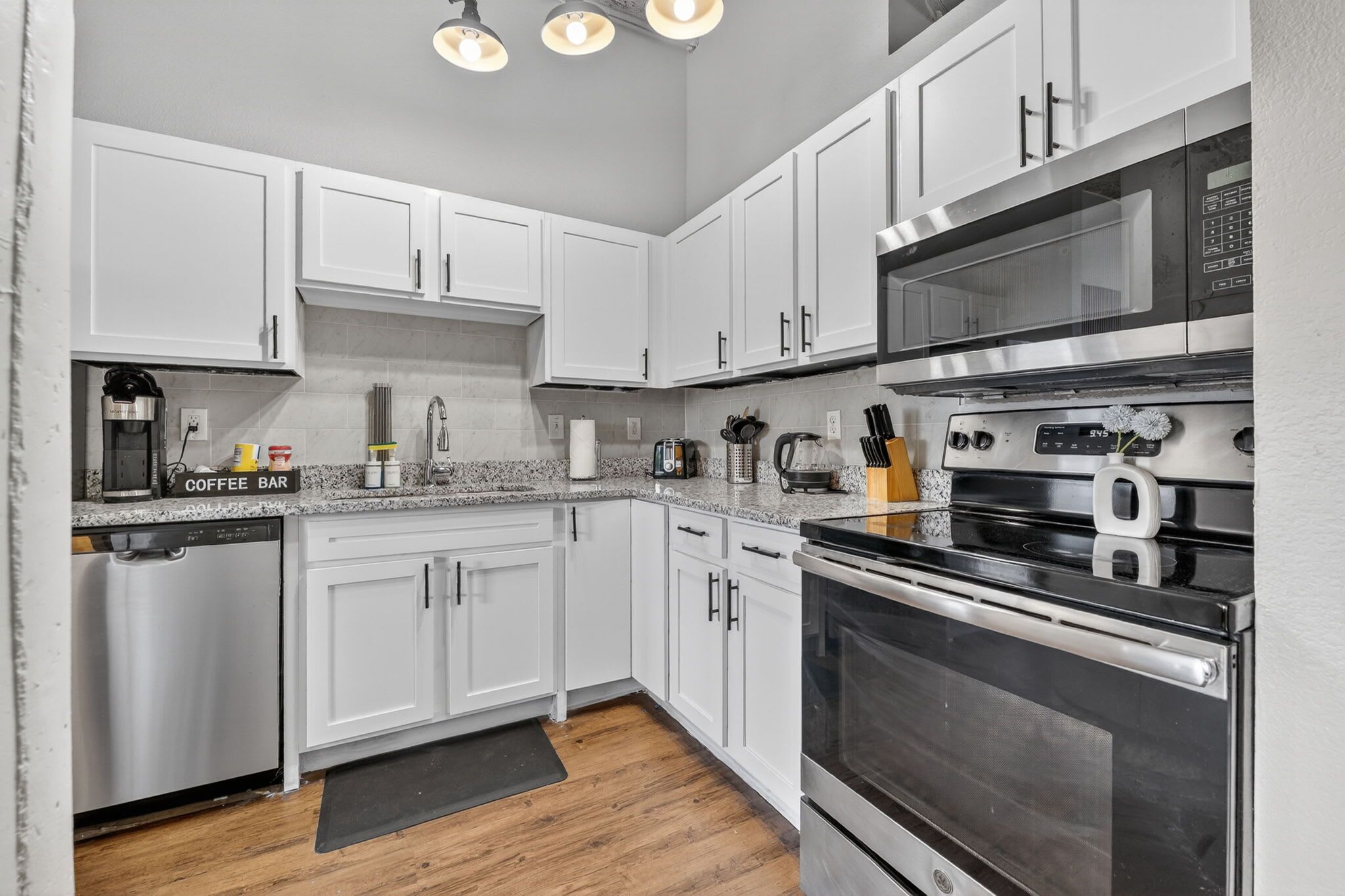 A modern kitchen with white cabinets, stainless steel appliances, and a coffee bar.