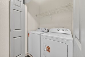A laundry room with two white washers and dryers, a metal drying rack, and a white door. - Urban River Market Escape | 2BR, Sleeps 6 (Kansas City)