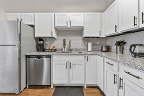 A modern kitchen with white cabinets, stainless steel appliances, and a coffee bar. - Urban River Market Escape | 2BR, Sleeps 6 (Kansas City)