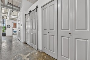A hallway with white doors, a brick wall, and a plant. - River Market Loft Stay - 2BR Stay Near Downtown KC (Kansas City)