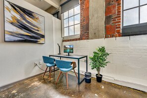 Une pièce comprenant un bureau, deux chaises, un écran d’ordinateur, une plante et un grand tableau abstrait accroché au mur.