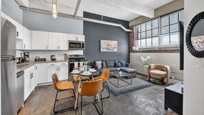 A modern kitchen with white cabinets, a dining area with orange chairs, and a gray sofa.