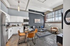 A modern kitchen with white cabinets, a dining area with orange chairs, and a gray sofa. - River Market Loft Stay - 2BR Stay Near Downtown KC (Kansas City)