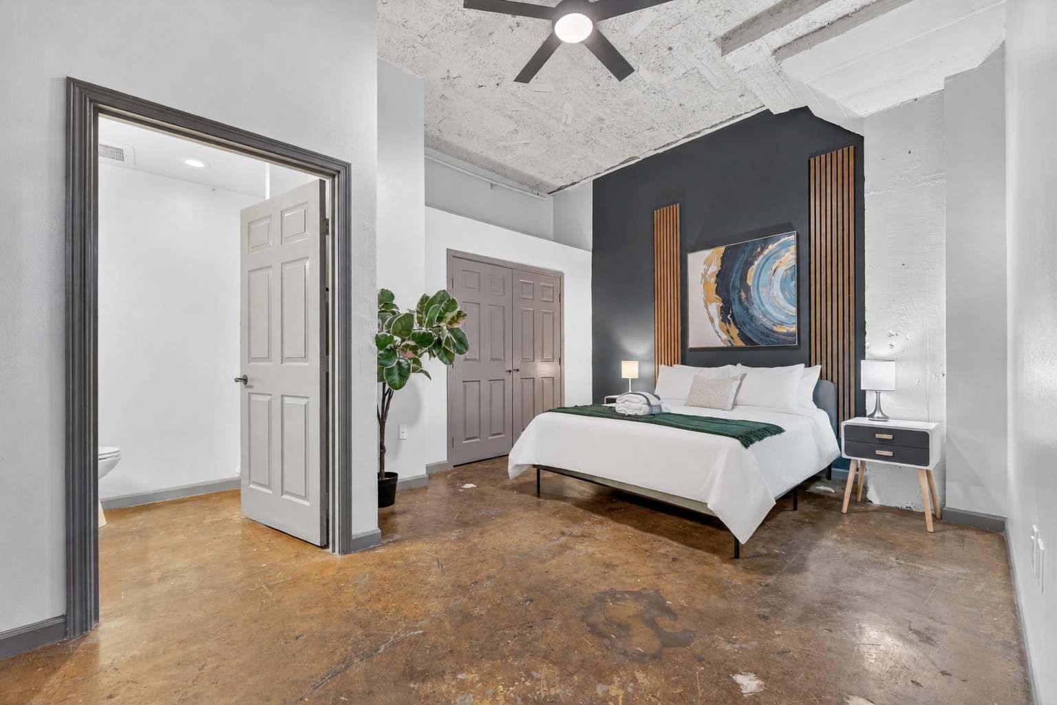 A bedroom with a bed, bedside tables, a ceiling fan, and a large abstract painting on the wall.