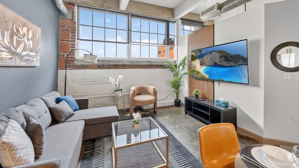 A modern living room with a sofa, armchair, coffee table, TV, and a large window.