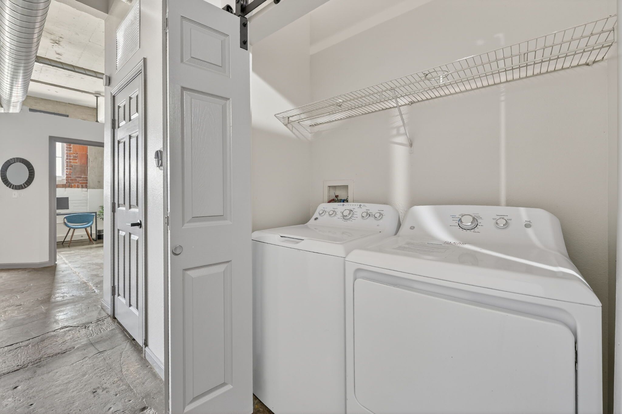 Una lavandería con dos lavadoras blancas, un tendedero y una puerta que da a otra habitación.