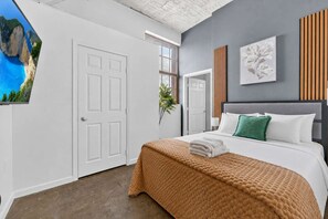 A bedroom with a bed, a door, a window, and a wall-mounted picture. - Downtown KC 2BR Loft with Parking & Fast WiFi (Kansas City)