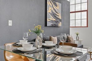 A modern dining area with a glass table, white plates, and a vase with yellow flowers. - Downtown KC 2BR Loft with Parking & Fast WiFi (Kansas City)
