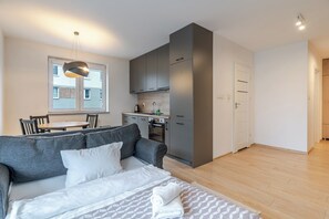 A modern apartment with a grey sofa, a dining table, a kitchen with grey cabinets, and a wooden floor. - Bogucice Modern Apartment (Katowice)