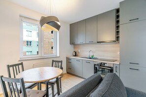 A modern kitchen with grey cabinets, a round wooden table, and a grey sofa. - Bogucice Modern Apartment (Katowice)