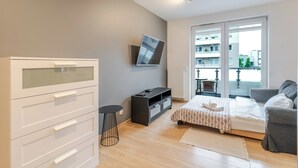 Camera da letto moderna con un letto, una televisione, una cassettiera e un balcone vista edifici.