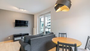 Un soggiorno moderno con un divano grigio, una televisione a schermo piatto, un tavolo da pranzo con sedie e una lampada a sospensione originale.