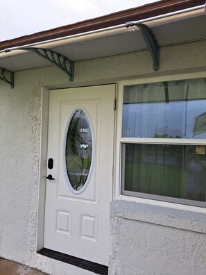 A white front door with a glass panel, a window with a curtain, and a metal gutter above. - Soothing 1-bedroom house with AC in vibrant Orlando (Orlando)