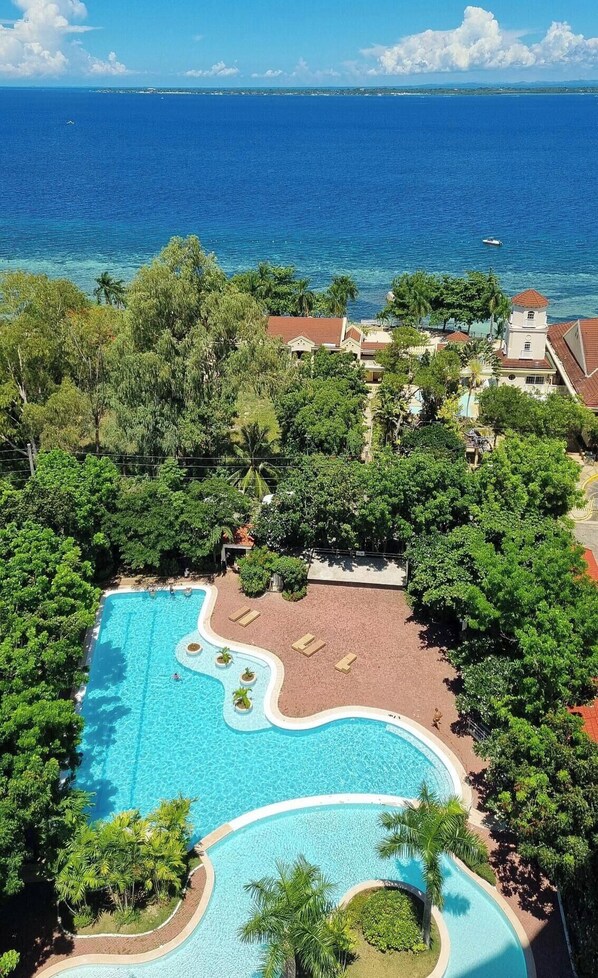 Blick vom Balkon eines Resorts mit Schwimmbad, üppiger Vegetation und Meerblick.