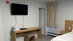 A hotel room with a bed, a desk with a chair, a television mounted on the wall, and a window with curtains. - Rundle Inn and Suites (Edmonton)
