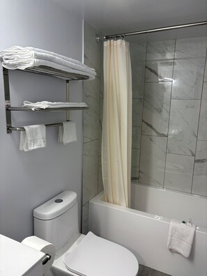 A bathroom with a toilet, a shower curtain, and towels on a rack. - Rundle Inn and Suites (Edmonton)