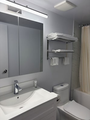 Un baño moderno con un espejo grande, un lavamanos blanco, un inodoro y una cortina de ducha.