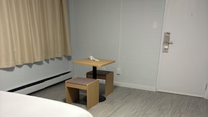 A hotel room with a bed, a small table with a phone, a chair, and a door. - Rundle Inn and Suites (Edmonton)