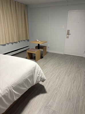 Habitació d'hotel amb un llit, una taula petita amb un telèfon, una cadira i una porta.