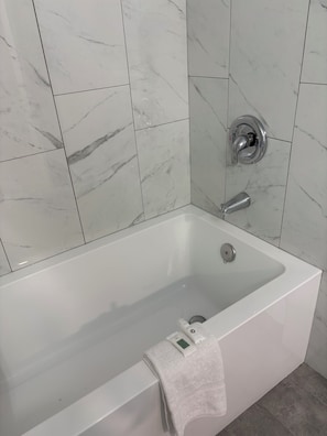 Un baño moderno con una bañera blanca, grifería cromada y baldosas de mármol.