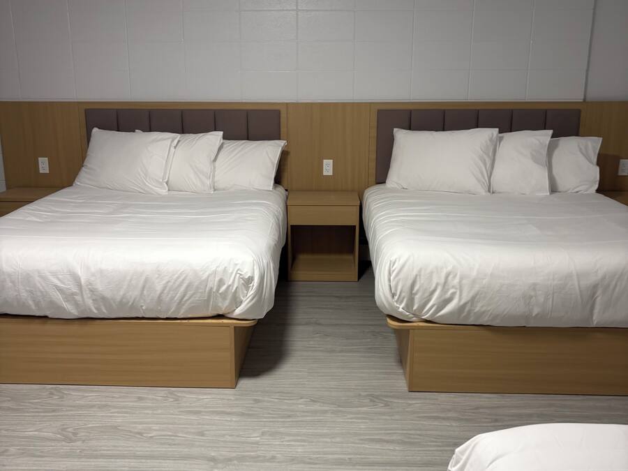Quarto de hotel com duas camas, cabeceiras de madeira e chão de madeira claro.