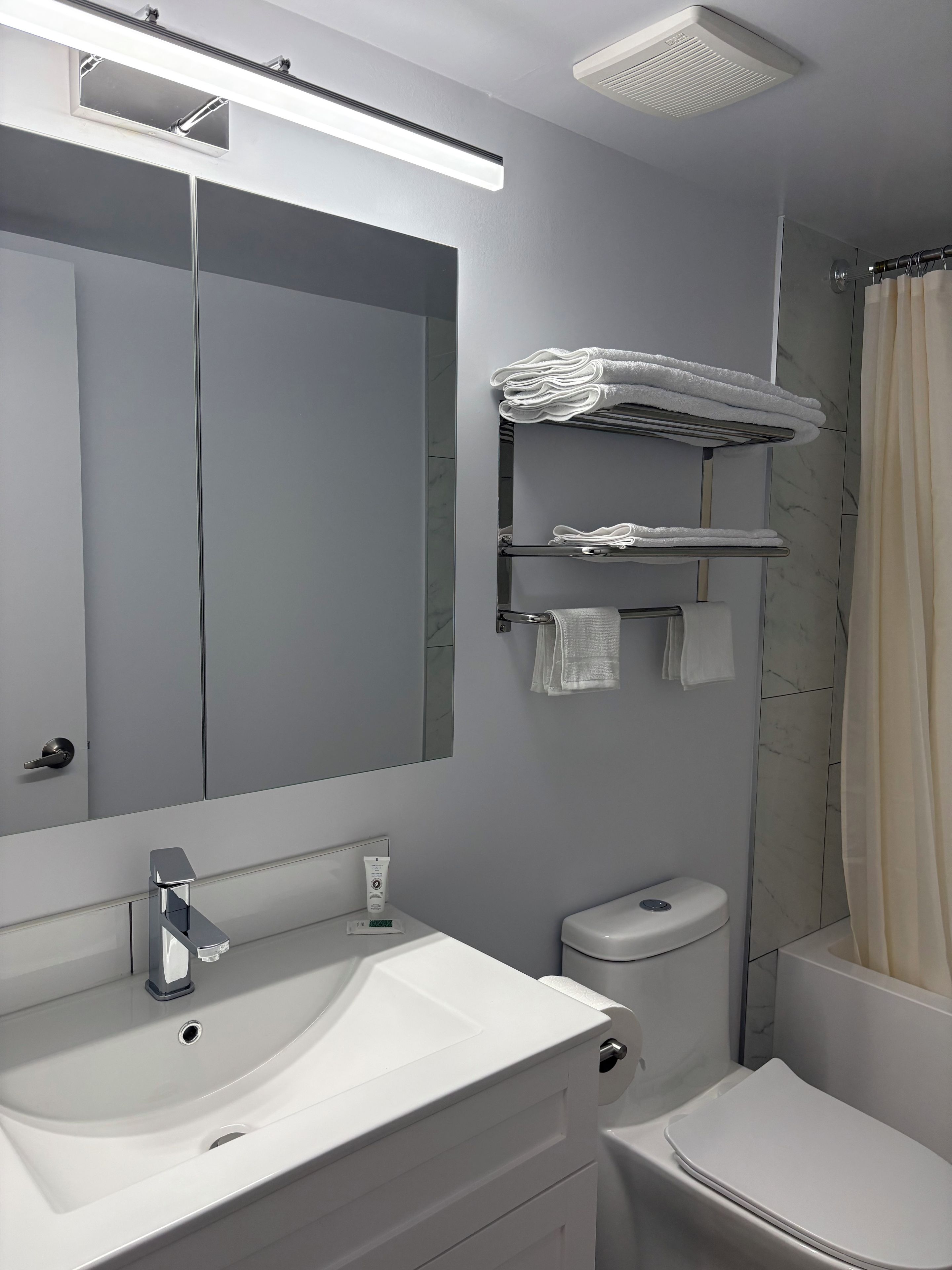 Un baño moderno con un espejo grande, un lavamanos blanco, un inodoro y una cortina de ducha.