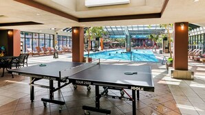 Zwei JoolA-Tischtennisplatten in einem hellen Innenbereich mit Pool und Liegestühlen.