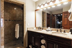 Un baño con un espejo grande, dos lavamanos, zona de ducha y un perchero para toallas.