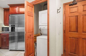 Una cocina con armarios de madera, un refrigerador de acero inoxidable, un microondas y una lavadora blanca.
