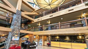 Eine mehrstöckige Hotelhalle mit Holzbalken, einer Steinsäule, einer Rezeption und einer großen Kandelaber.