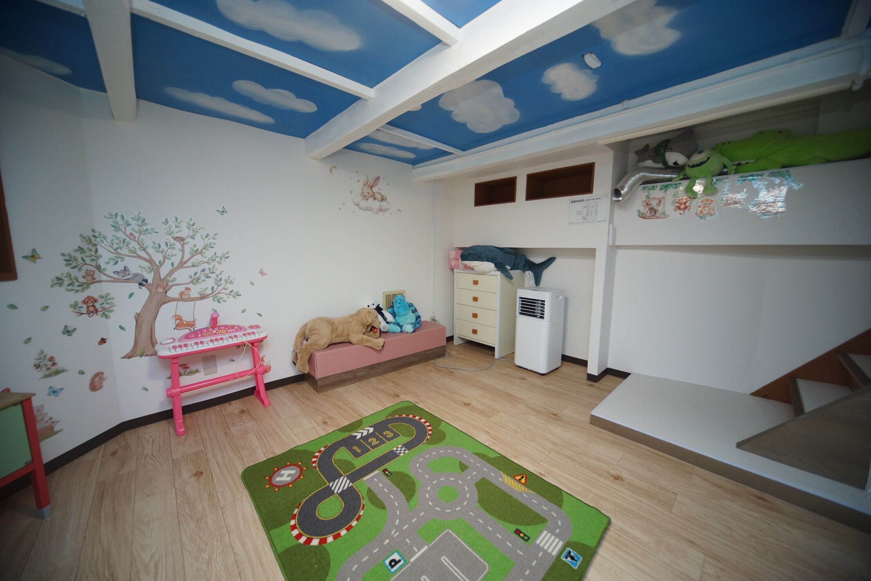 A child's room with a bunk bed, a play mat, a small table, and a wall with a tree and animal decals.