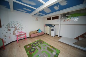 Kinderzimmer mit Etagenbett, Spielmatte, kleinem Tisch und Wand mit Bäume- und Tieraufklebern.