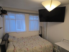 Ein Schlafzimmer mit einem Bett, einem Schreibtisch, einem Stuhl, einem Fernseher und einem Fenster mit Vorhängen.